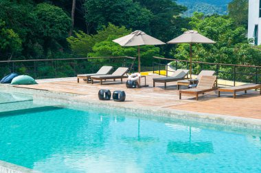 Dağ ve mavi gökyüzü arkaplanlı yüzme havuzunun etrafında şemsiyeli yatak havuzu