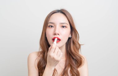 Güzel Asyalı kadın portresi makyaj yapıyor ve beyaz arka planda kırmızı ruj kullanıyor.