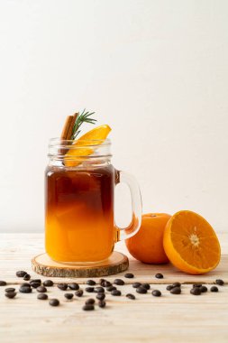 Bir bardak buzlu americano sade kahve ve ahşap arka planda biberiye ve tarçınla süslenmiş portakal ve limon suyu.