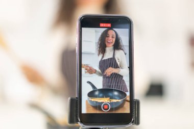 Latin kadın blogda paylaşmak için mutfakta video ve yemek çekiyor.