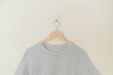 grey t-shirt hanging with wood hanger on wall