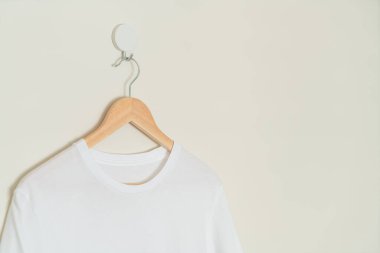 white t-shirt hanging with wood hanger on wall