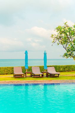 Sandalye havuzu ve şemsiyeyle okyanus arka planında yüzme havuzu