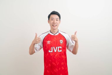 Bangkok, THAILAND - 27 Kasım 2021: beyaz arka planda Arsenal tişörtü giyen genç Asyalı. Arsenal, Londra 'nın en ünlü futbol kulübüdür..