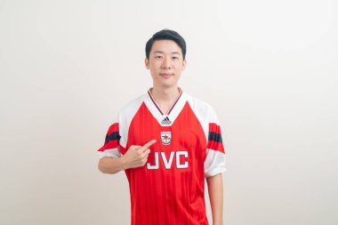 Bangkok, THAILAND - 27 Kasım 2021: beyaz arka planda Arsenal tişörtü giyen genç Asyalı. Arsenal, Londra 'nın en ünlü futbol kulübüdür..