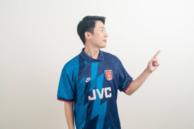 Bangkok, THAILAND - 27 Kasım 2021: beyaz arka planda Arsenal tişörtü giyen genç Asyalı. Arsenal, Londra 'nın en ünlü futbol kulübüdür..