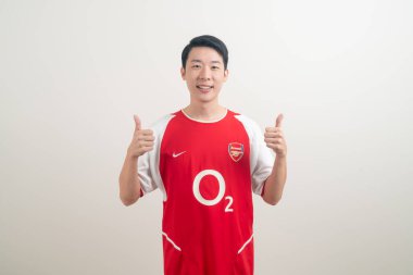 Bangkok, THAILAND - 27 Kasım 2021: beyaz arka planda Arsenal tişörtü giyen genç Asyalı. Arsenal, Londra 'nın en ünlü futbol kulübüdür..
