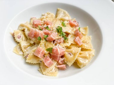 Beyaz tabakta jambonlu carbonara farfelle makarnası.