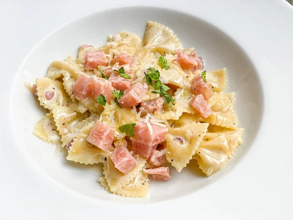 Beyaz tabakta jambonlu carbonara farfelle makarnası.