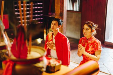 Mutlu genç Asyalı çift, geleneksel Çin elbiseleriyle Çin tapınağında dua ederek sevişiyor.