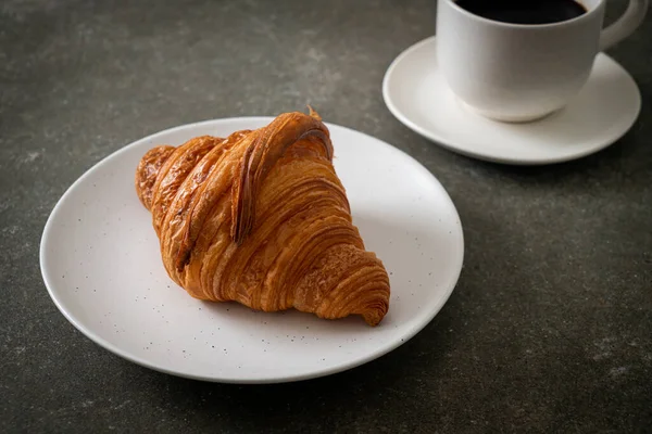 Beyaz tabakta taze kruvasan ve siyah kahve.