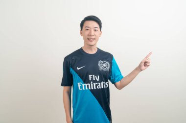 Bangkok, THAILAND - 27 Kasım 2021: beyaz arka planda Arsenal tişörtü giyen genç Asyalı. Arsenal, Londra 'nın en ünlü futbol kulübüdür..