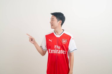 Bangkok, THAILAND - 27 Kasım 2021: beyaz arka planda Arsenal tişörtü giyen genç Asyalı. Arsenal, Londra 'nın en ünlü futbol kulübüdür..