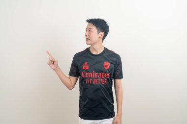 Bangkok, THAILAND - 27 Kasım 2021: beyaz arka planda Arsenal tişörtü giyen genç Asyalı. Arsenal, Londra 'nın en ünlü futbol kulübüdür..