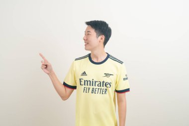 Bangkok, THAILAND - 27 Kasım 2021: beyaz arka planda Arsenal tişörtü giyen genç Asyalı. Arsenal, Londra 'nın en ünlü futbol kulübüdür..