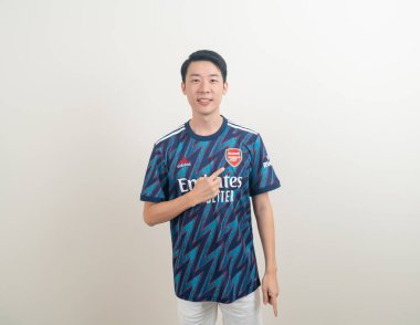 Bangkok, THAILAND - 27 Kasım 2021: beyaz arka planda Arsenal tişörtü giyen genç Asyalı. Arsenal, Londra 'nın en ünlü futbol kulübüdür..