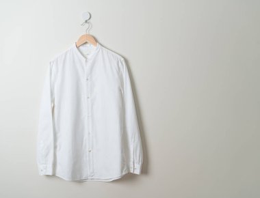 Duvarında ahşap askı olan beyaz gömlek asılı.