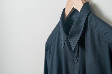 Duvarında ahşap askı olan siyah bir gömlek asıyor.