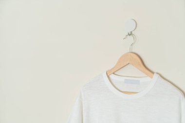 white t-shirt hanging with wood hanger on wall
