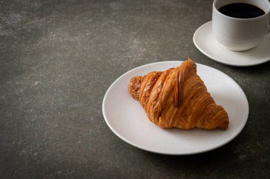 Beyaz tabakta taze kruvasan ve siyah kahve.