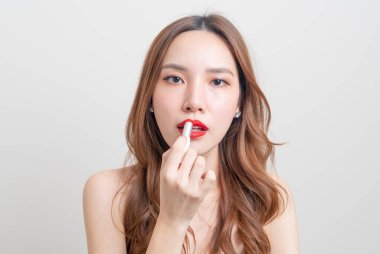 Güzel Asyalı kadın portresi makyaj yapıyor ve beyaz arka planda kırmızı ruj kullanıyor.