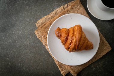 Beyaz tabakta taze kruvasan ve siyah kahve.