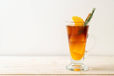 Bir bardak buzlu americano sade kahve ve ahşap arka planda biberiye ve tarçınla süslenmiş portakal ve limon suyu.