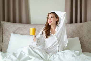 Portre güzel Asyalı kadın uyanır ve elinde kahve fincanı ya da kupayla sabah uyanır.