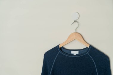 navy sweater hanging with wood hanger on wall