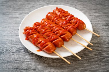 Beyaz tabakta ketçaplı kızarmış sosis şişi.