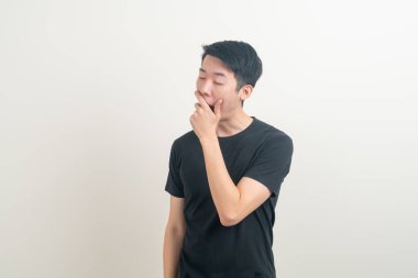 Esnemiş suratlı ve beyaz arka planda uykulu genç bir Asyalı.