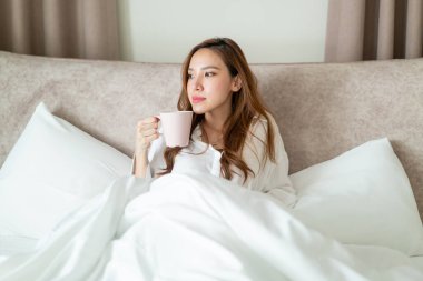 Portre güzel Asyalı kadın uyanır ve elinde kahve fincanı ya da kupayla sabah uyanır.
