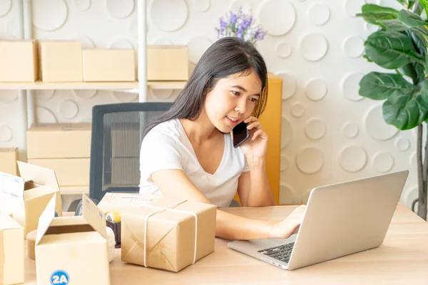 Asyalı bir kadın internette dizüstü bilgisayar ve ofis telefonlarını kullanırken eğleniyor - online veya çevrimiçi alışveriş kavramı satmak