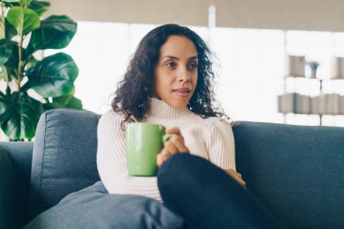 Latin kadın evdeki kanepede kahve içiyor.
