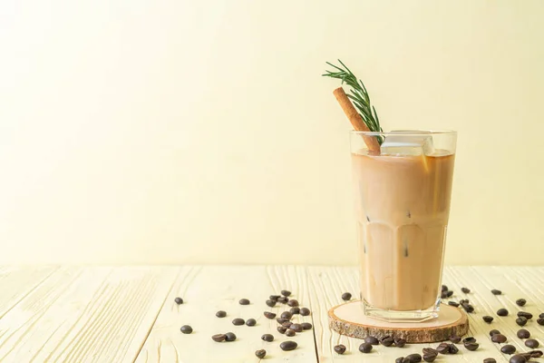 pouring milk in black coffee glass with ice cube, cinnamon and rosemary on wood background