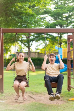 Asian couple love play on the swing in kids playground