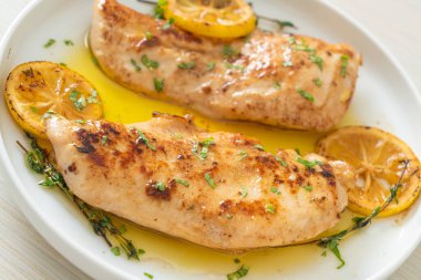 Beyaz tabakta tereyağlı ızgara tavuk, limon ve sarımsak.