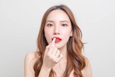 Güzel Asyalı kadın portresi makyaj yapıyor ve beyaz arka planda kırmızı ruj kullanıyor.