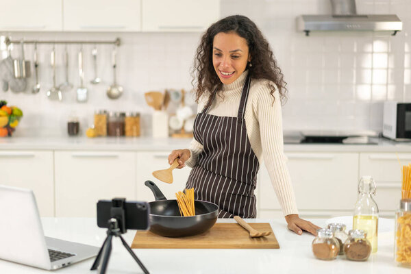 Latin woman shooting video and cooking at the kitchen for share on blog