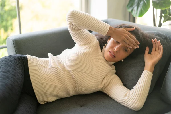 Latin kadın evdeki kanepede uzanmış baş ağrısı çekiyor.