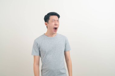 Esnemiş suratlı ve beyaz arka planda uykulu genç bir Asyalı.