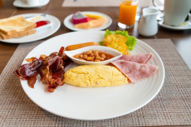 breakfast set - omelette, bacon, ham, sausages, fresh vegetable salad on plate in morning time - Hotel breakfast set concept