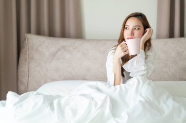 Portre güzel Asyalı kadın uyanır ve elinde kahve fincanı ya da kupayla sabah uyanır.