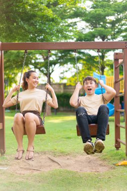 Asian couple love play on the swing in kids playground