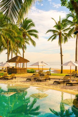 Otelde açık havuzda güzel bir şemsiye ve sandalye ve gün batımında hindistan cevizi palmiyesi ağacı olan bir tatil ve tatil konsepti.