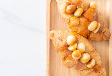 Macadamia ve ahşap tabakta karamel ile kruvasan.