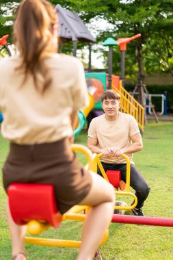 Asian couple love play seesaw with smiling in kids playground