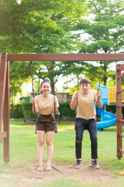 Asian couple love play on the swing in kids playground