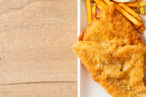 fish and chips - fried fish fillet with potatoes chips and lemon on white plate