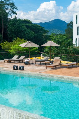 Dağ ve mavi gökyüzü arkaplanlı yüzme havuzunun etrafında şemsiyeli yatak havuzu